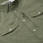 Close-up of The Grazer | Poncho, an olive green work shirt by Poncho, featuring front flap pockets with silver snap buttons and a small black "Poncho" label on the left pocket.