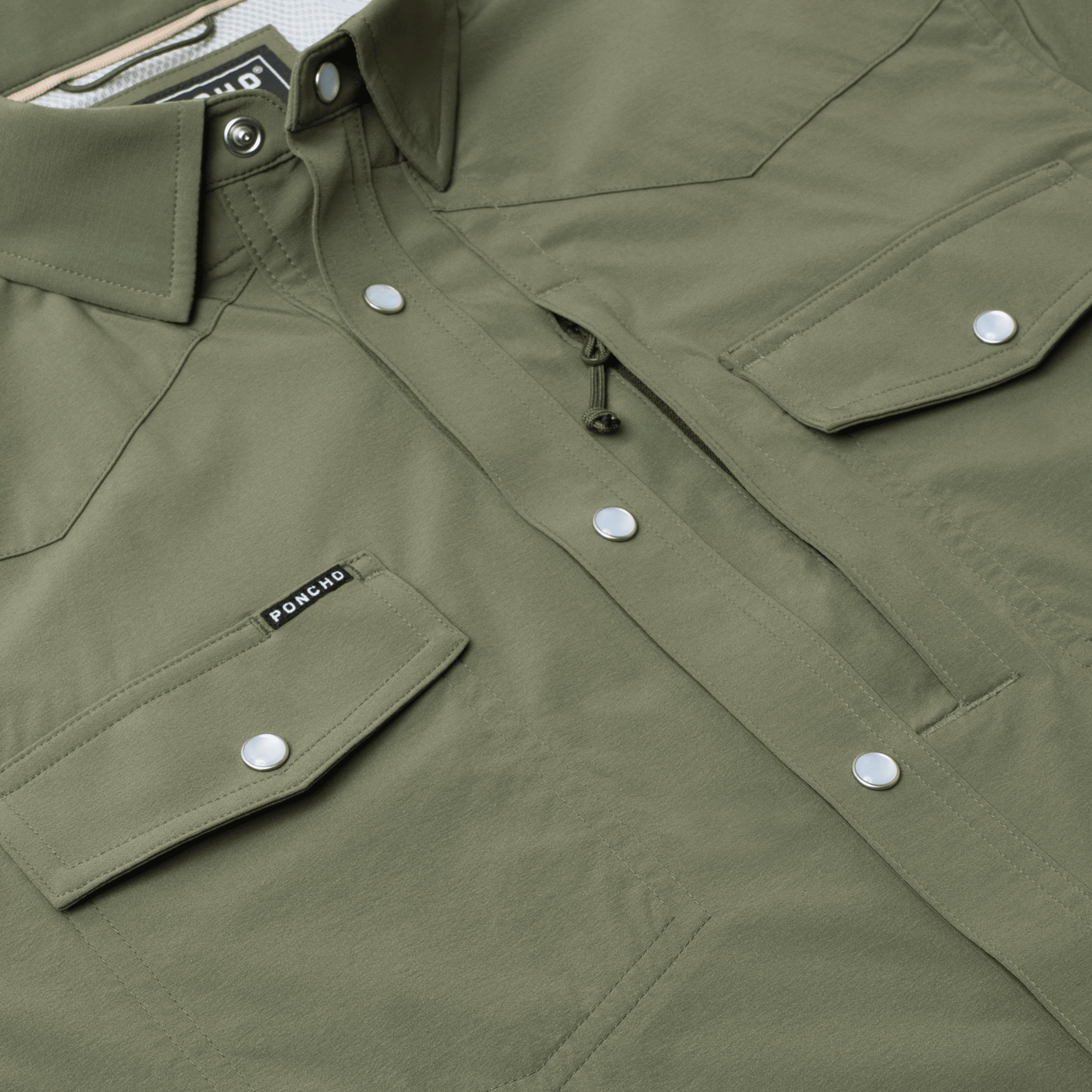 Close-up of The Grazer | Poncho, an olive green work shirt by Poncho, featuring front flap pockets with silver snap buttons and a small black "Poncho" label on the left pocket.