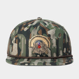 The Duck Camp Grandpa Hat — Turkey is an adjustable snapback cap featuring a camouflage design and an embroidered turkey patch on the front panel, highlighted by a curved rope accent above the brim. This hat from Duck Camp blends rugged style with a customizable, comfortable fit.