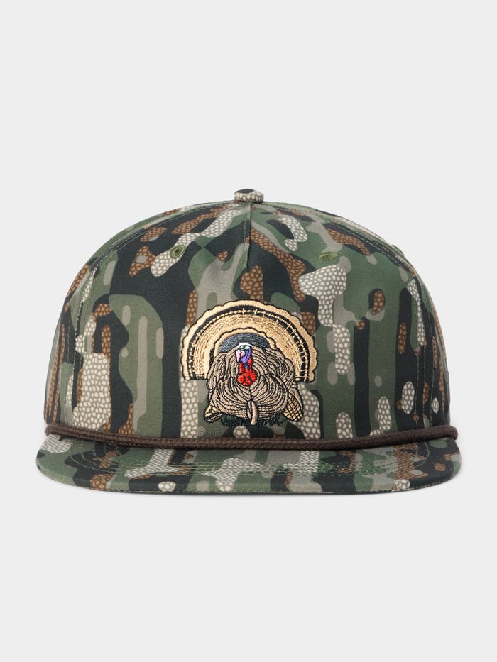 The Duck Camp Grandpa Hat — Turkey is an adjustable snapback cap featuring a camouflage design and an embroidered turkey patch on the front panel, highlighted by a curved rope accent above the brim. This hat from Duck Camp blends rugged style with a customizable, comfortable fit.