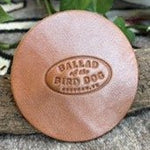 Add a touch of style to any space with the Ballad of the Bird Dog 5 Pack Leather Coaster, featuring a round leather patch embossed with “Ballad of the Bird Dog, Brenham, TX.” Each coaster rests on a textured surface and is accented with leaves in the background—ideal as handmade coasters or stylish desk accessories for any setting.