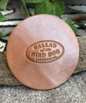 Add a touch of style to any space with the Ballad of the Bird Dog 5 Pack Leather Coaster, featuring a round leather patch embossed with “Ballad of the Bird Dog, Brenham, TX.” Each coaster rests on a textured surface and is accented with leaves in the background—ideal as handmade coasters or stylish desk accessories for any setting.