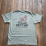Light gray Bird Dog Series Shirt | Brittany by Ballad Originals on wooden floor, featuring an illustration of a Brittany dog with the text: “True Companionship. BRITTANY. Ballad of the Bird Dog.” Ideal for those who value loyal hunting companions, this tee honors the unique bond between owner and pup.