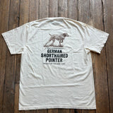 A cream-colored Bird Dog Series Shirt | German Shorthaired Pointer by Ballad Originals lies flat on a wooden floor, featuring a graphic of a dog and the text: “True Companionship, German Shorthaired Pointer, Ballad of the Bird Dog.” Perfect for any bird dog enthusiast, this tee is an ideal hunting shirt or everyday favorite.