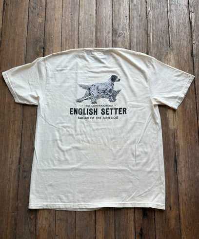 The Bird Dog Series Shirt | English Setter from Ballad Originals is a cream-colored Comfort Colors tee, photographed on a wooden floor. It features an illustration of an English Setter dog and “The Companionable English Setter Ballad of the Bird Dog” printed on the back—perfect for anyone who wants to showcase their love for classic style and their favorite hunting companion.