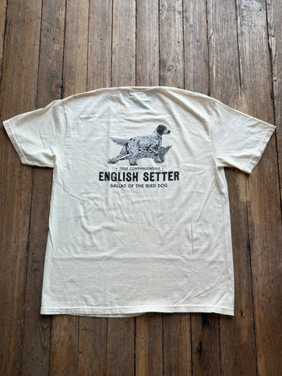 The Bird Dog Series Shirt | English Setter from Ballad Originals is a cream-colored Comfort Colors tee, photographed on a wooden floor. It features an illustration of an English Setter dog and “The Companionable English Setter Ballad of the Bird Dog” printed on the back—perfect for anyone who wants to showcase their love for classic style and their favorite hunting companion.