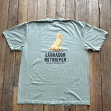 Showcased on a wooden floor, the Ballad Originals Bird Dog Series Shirt | Labrador Retriever features a soft gray Comfort Colors tee with a yellow Labrador Retriever graphic and “Labrador Retriever, Sailor of the Bird Dog” printed on the back—a perfect tribute to loyal hunting companions.