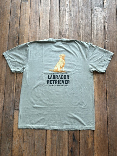 Showcased on a wooden floor, the Ballad Originals Bird Dog Series Shirt | Labrador Retriever features a soft gray Comfort Colors tee with a yellow Labrador Retriever graphic and “Labrador Retriever, Sailor of the Bird Dog” printed on the back—a perfect tribute to loyal hunting companions.