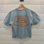 Yankey blue Small Town Revival Crop Ballad of the Bird Dog t-shirt with an orange graphic on the back that reads “Small Town Revival, Brenham Texas” inside a rectangular border.
