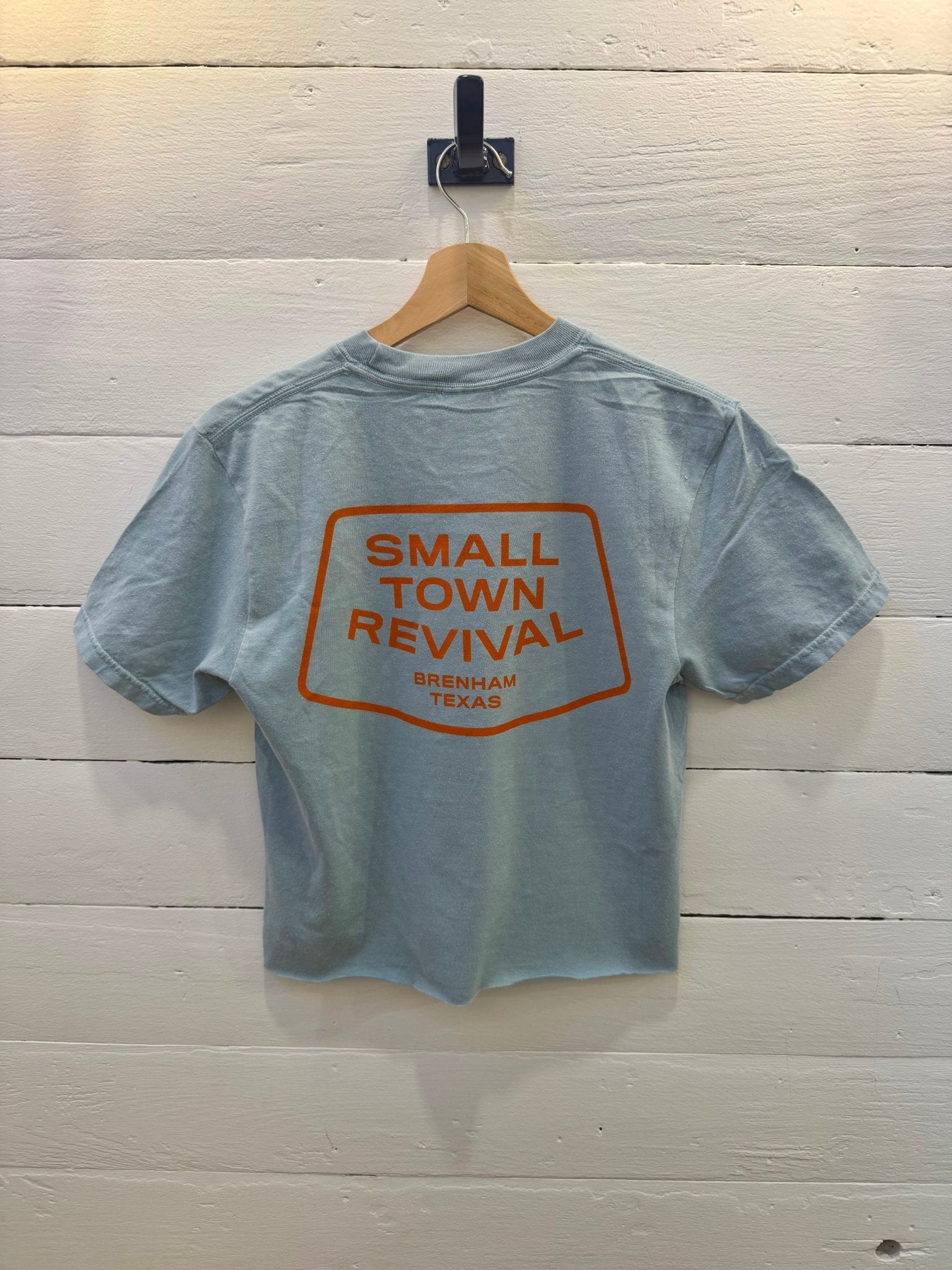 Yankey blue Small Town Revival Crop Ballad of the Bird Dog t-shirt with an orange graphic on the back that reads “Small Town Revival, Brenham Texas” inside a rectangular border.