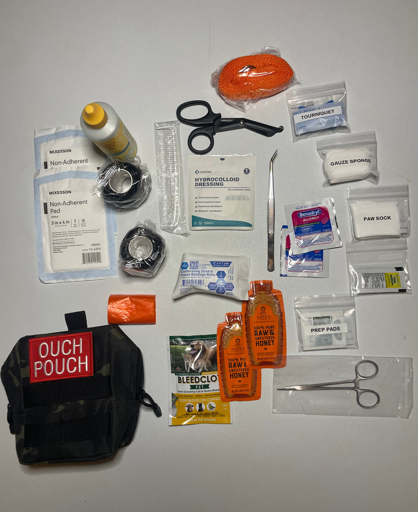 The CoveyKits Molle Kit- Working Dog First Aid Kit is displayed with its contents spread out, showcasing pet wound care essentials such as bandages, scissors, tweezers, gauze, a tourniquet, prep pads, honey packets, a paw sock, and a compact pouch labeled “Ouch Pouch.”.