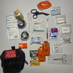 The CoveyKits Molle Kit- Working Dog First Aid Kit is displayed with its contents spread out, showcasing pet wound care essentials such as bandages, scissors, tweezers, gauze, a tourniquet, prep pads, honey packets, a paw sock, and a compact pouch labeled “Ouch Pouch.”.