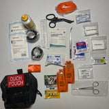 The CoveyKits Molle Kit- Working Dog First Aid Kit is displayed with its contents spread out, showcasing pet wound care essentials such as bandages, scissors, tweezers, gauze, a tourniquet, prep pads, honey packets, a paw sock, and a compact pouch labeled “Ouch Pouch.”.