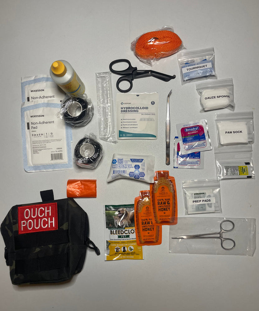 The CoveyKits Molle Kit- Working Dog First Aid Kit is displayed with its contents spread out, showcasing pet wound care essentials such as bandages, scissors, tweezers, gauze, a tourniquet, prep pads, honey packets, a paw sock, and a compact pouch labeled “Ouch Pouch.”.