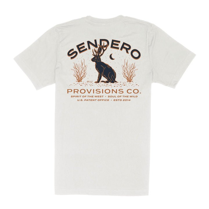 The Jackalope Pocket Tee by Sendero Provisions Co. is a white organic cotton t-shirt featuring a jackalope, plants, moon graphic, “Sendero Provisions Co.” text, and branded details.