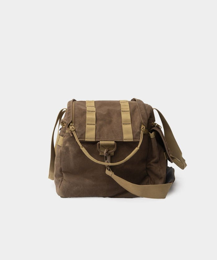 Duck Camp Canvas Blind Bag in brown waxed canvas with tan straps and buckle closure, featuring a detachable padded shoulder strap, displayed against a plain white background.