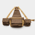 The Duck Camp Canvas Upland Strap Vest by Duck Camp is shown on a plain white background, featuring a brown and tan design with three compartments, adjustable beige straps inspired by classic field gear, and secure snap button closures.