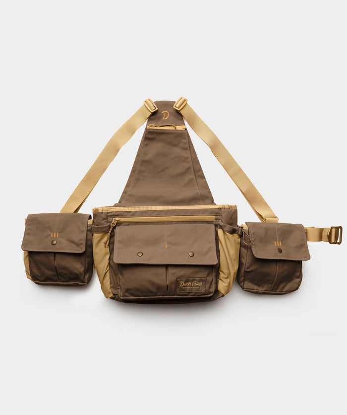 The Duck Camp Canvas Upland Strap Vest by Duck Camp is shown on a plain white background, featuring a brown and tan design with three compartments, adjustable beige straps inspired by classic field gear, and secure snap button closures.