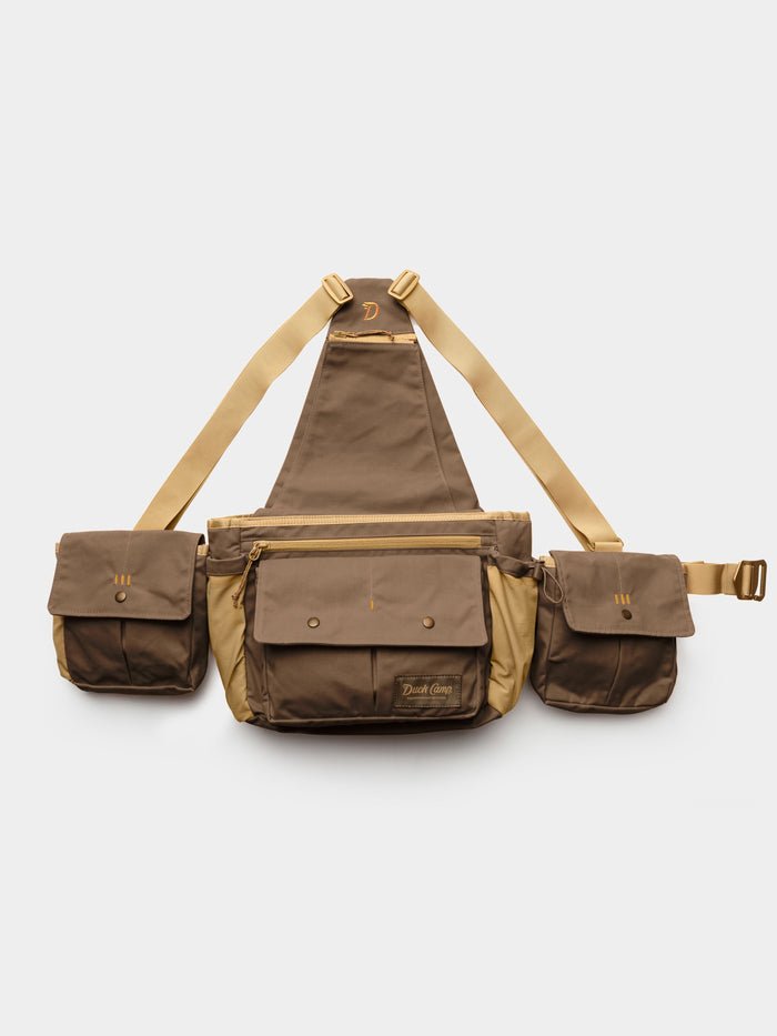 The Duck Camp Canvas Upland Strap Vest by Duck Camp is shown on a plain white background, featuring a brown and tan design with three compartments, adjustable beige straps inspired by classic field gear, and secure snap button closures.