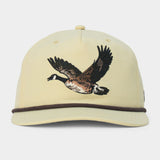 The Canada Goose Hat by Duck Camp is a light yellow, classic 5-panel baseball cap featuring an embroidered flying goose on the front and a dark brown cord above the brim, complete with an adjustable snapback for a perfect fit.
