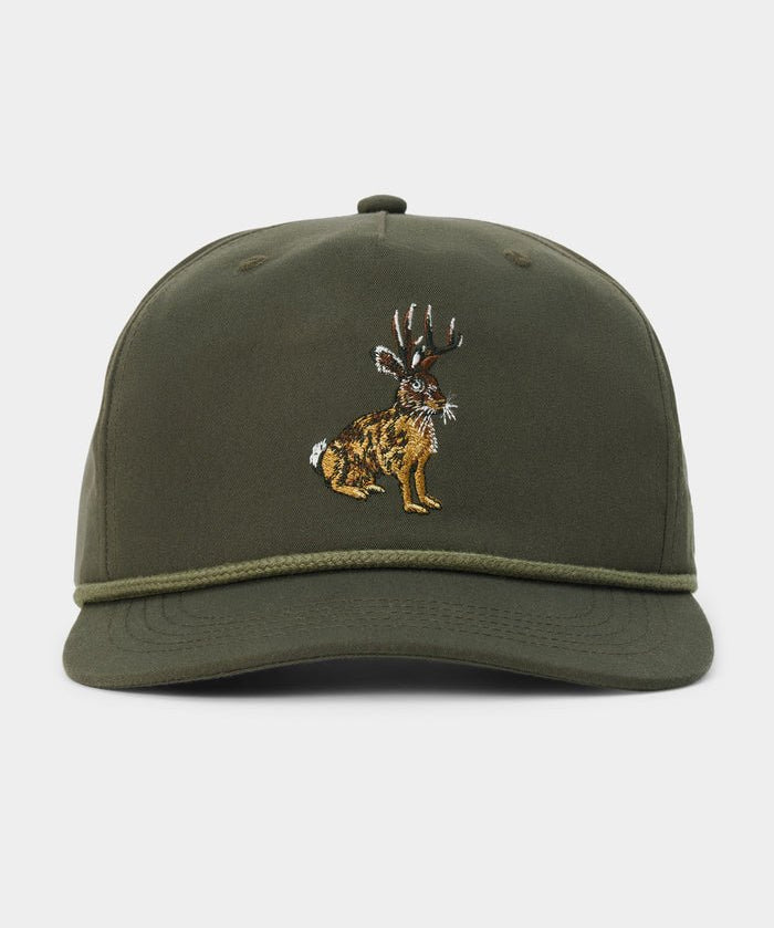 The Duck Camp Jackalope Hat is an olive green baseball cap featuring an embroidered jackalope design on the front, a decorative cord above the brim, and an adjustable snapback for a comfortable fit.