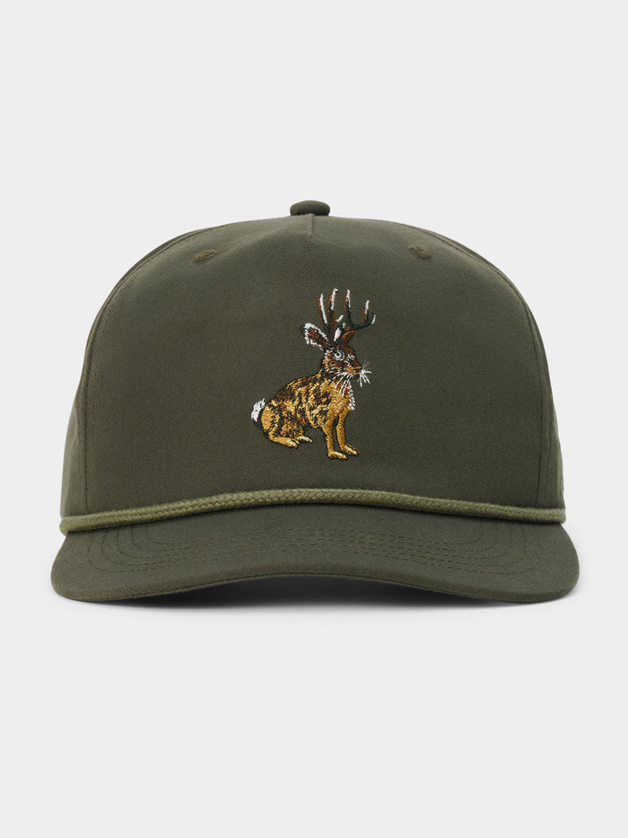 The Duck Camp Jackalope Hat is an olive green baseball cap featuring an embroidered jackalope design on the front, a decorative cord above the brim, and an adjustable snapback for a comfortable fit.