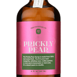 A brown glass bottle with a pink label reading "Prickly Pear Syrup | Yes Cocktail Co" contains a vibrant syrup made from real prickly pear juice, perfect for cocktails, crafted by Yes Cocktail Co.