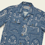 The Shores Club Shirt by Howler Brothers is a 100% cotton blue camp collar shirt with a white palm and floral pattern, vintage textured weave, two flap chest pockets, and brown buttons.