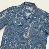 The Shores Club Shirt by Howler Brothers is a 100% cotton blue camp collar shirt with a white palm and floral pattern, vintage textured weave, two flap chest pockets, and brown buttons.