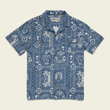 The Shores Club Shirt by Howler Brothers is a short-sleeve blue camp collar shirt with white tropical prints, featuring palm trees and geometric patterns. Made from 100% cotton with a vintage textured weave, shown laid flat on a plain background.