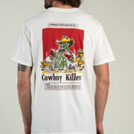 A man wearing the Cowboy Killers T-Shirt by Sendero Provisions Co.—a white organic cotton tee featuring a cartoon cactus with boxing gloves and “Cowboy Killers” printed on the back, finished with a soft-touch screen print for lasting comfort.