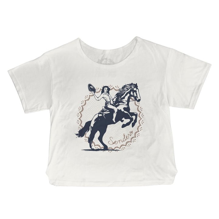 The Palomino Basic Tee by Sendero Provisions Co. features a white, relaxed oversized fit with a navy graphic of a cowgirl riding a rearing horse and holding a hat, surrounded by “Sendero” script and a decorative border. Crafted from a soft cotton-polyester blend for all-day comfort.