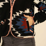 Close-up of a person with their hand in the pocket of a vintage black, blue, and red Sedona Fleece by Sendero Provisions Co. with light pink trim.