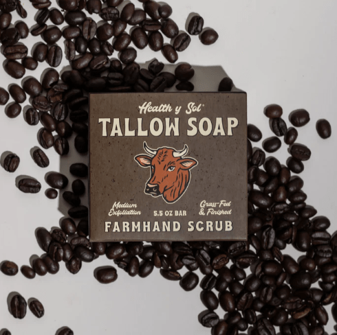 A box of Health y Sol Tallow Soap from Health y Sol, Farmhand Scrub variety, made with all-natural ingredients, is displayed on a white surface with scattered coffee beans.