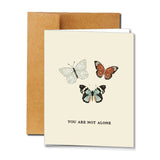 Not Alone | Card by Ramble & Company features three illustrated butterflies above the phrase “YOU ARE NOT ALONE.” This uplifting comfort card comes with a brown envelope and is designed to remind someone special that they are never alone.