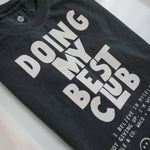 Black vintage faded t-shirt from Ramble & Company featuring bold white “DOING MY BEST CLUB” text, smaller lettering at the bottom, and a smiley face graphic. The Doing My Best Club tee offers a boxy, relaxed silhouette for effortless laid-back style.
