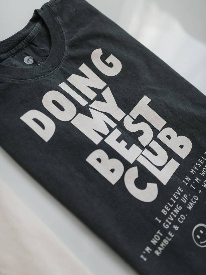 Black vintage faded t-shirt from Ramble & Company featuring bold white “DOING MY BEST CLUB” text, smaller lettering at the bottom, and a smiley face graphic. The Doing My Best Club tee offers a boxy, relaxed silhouette for effortless laid-back style.