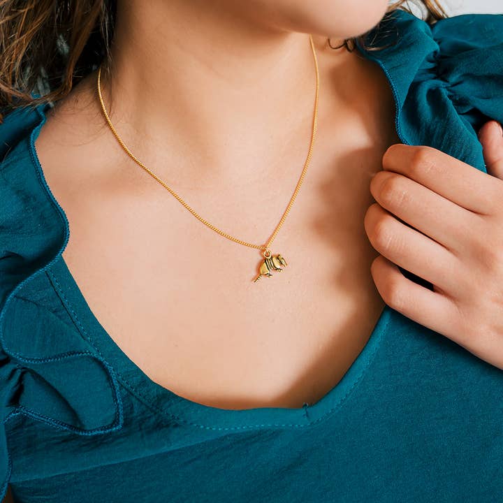 A person in a teal top wears an Armadillo Necklace, a gold curb chain featuring a small armadillo pendant.