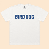Bird Dog Honor Shirt by Ballad Originals—crafted from premium USA cotton, this white shirt features “BIRD DOG” printed in bold blue letters across the chest and is displayed flat on a light beige background. A must-have for enthusiasts of classic hunting apparel.