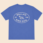 The Bird Dog Emblem Shirt by Ballad Originals features a blue design with an oval graphic on the back that reads “Ballad of the Bird Dog” and showcases a simple dog illustration at the center—perfect for displaying your bird dog pride while supporting local business.