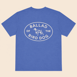 The Bird Dog Emblem Shirt by Ballad Originals features a blue design with an oval graphic on the back that reads “Ballad of the Bird Dog” and showcases a simple dog illustration at the center—perfect for displaying your bird dog pride while supporting local business.