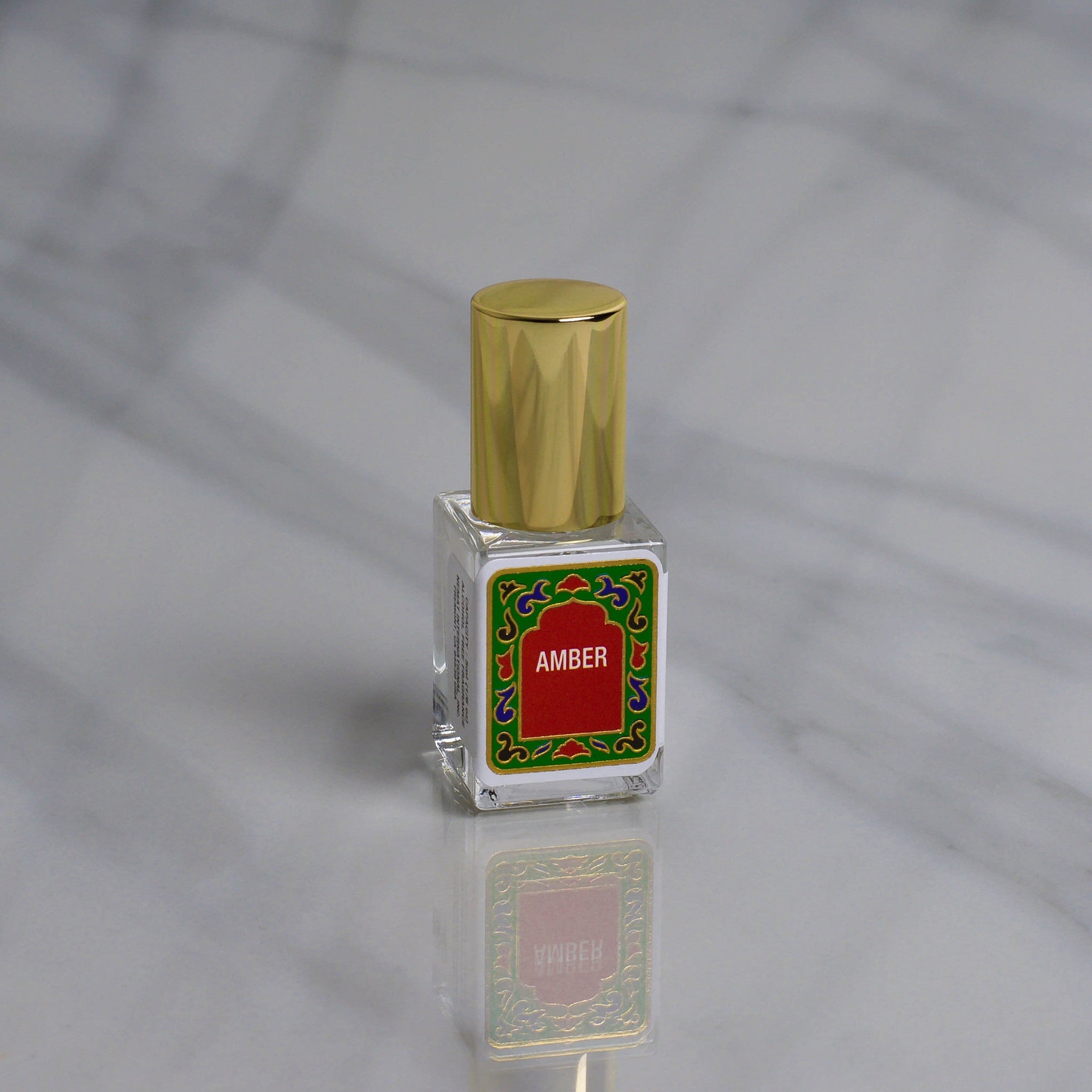 A small Nemat Amber Perfume Oil bottle with a gold cap and red label rests on marble, ready to reveal its subtle amber fragrance as your new signature scent.