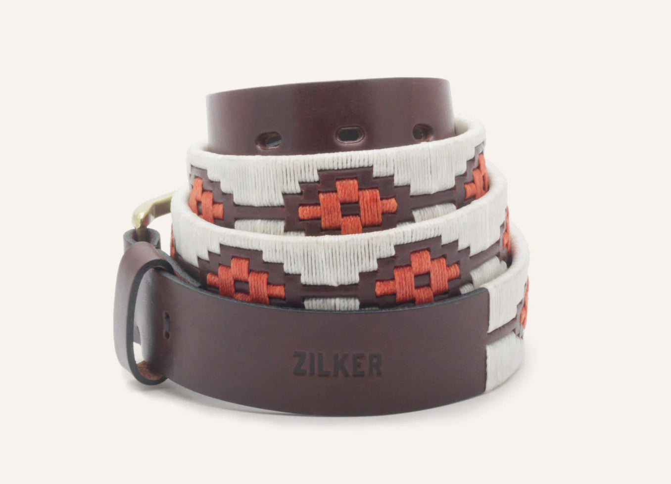 The ATX Dark by Zilker Belts is an Argentine leather belt with "ZILKER" embossed on the tip, hand-stitched white and red geometric embroidery, and a brass buckle.