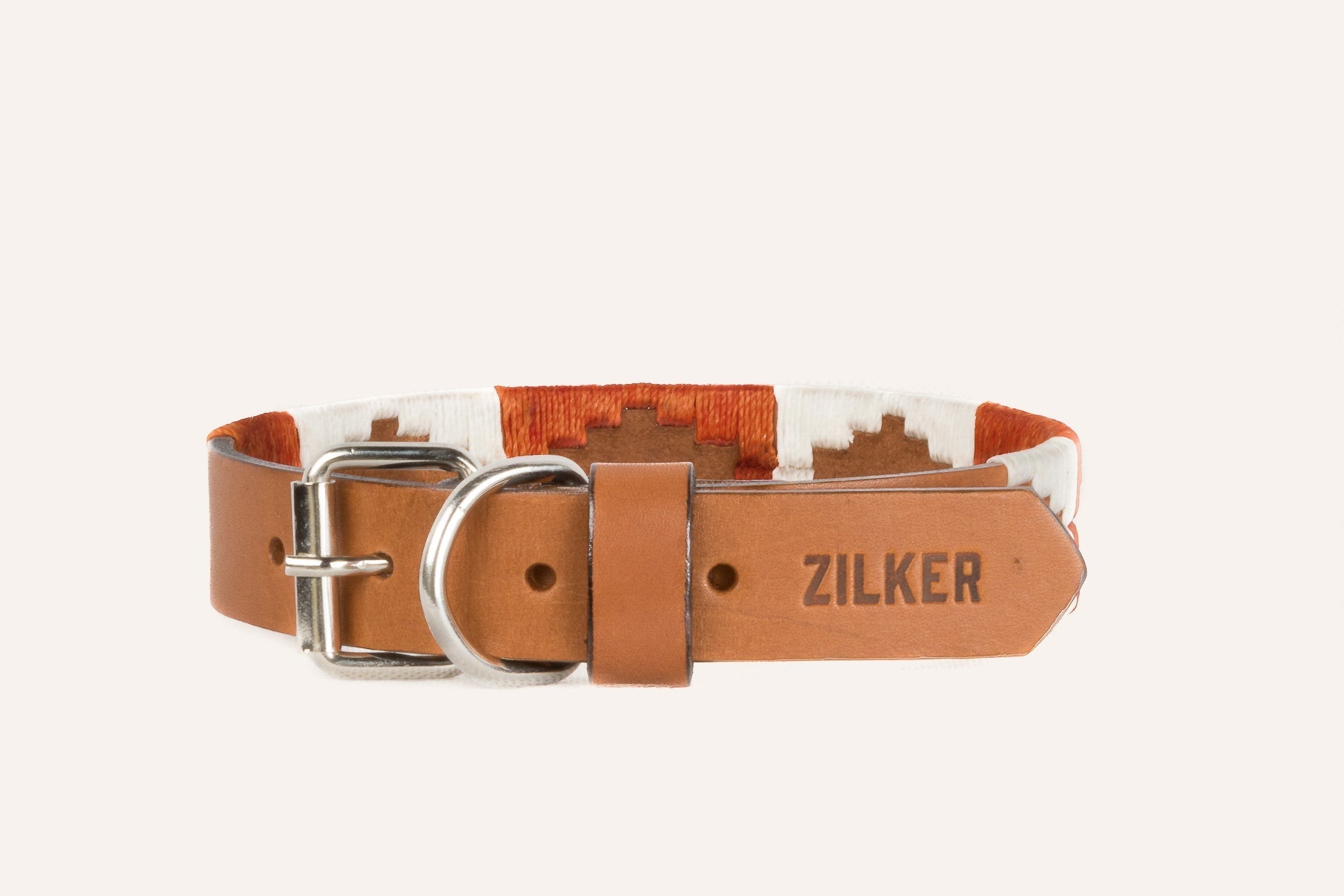 The ATX Dog Collar by Zilker Belts features a brown and white pattern, hand-stitched Argentine leather, a metal buckle, and "ZILKER" embossed on the leather end.