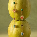 Bellevie Boho Gemstone Drop Earrings by Flanerie by MAIQ: two 18K gold chain drop earrings featuring multicolored circular and teardrop-shaped gemstones, suspended in front of two stacked pears.