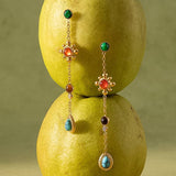 Bellevie Boho Gemstone Drop Earrings by Flanerie by MAIQ: two 18K gold chain drop earrings featuring multicolored circular and teardrop-shaped gemstones, suspended in front of two stacked pears.