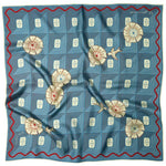 The Jenni Earle Silk Scarf - ‘But What If You Fly’ features a geometric square design in blue silk, accented with cream flowers and delicate birds. Inspired by classic western style, this giftable square neck or hair scarf is finished with a red wavy border and displays natural folds in the luxurious fabric.