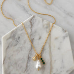 Introducing the Pearl, Cz Emerald, Star Charm Necklace by Mesa Blue—a refined 18K gold-plated chain showcasing a freshwater pearl pendant, a gold star charm, and three sparkling CZ emerald gemstones. Beautifully presented on a marble hexagon slab, this elegant necklace from Mesa Blue effortlessly elevates any look with its sophisticated design.