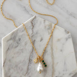 Introducing the Pearl, Cz Emerald, Star Charm Necklace by Mesa Blue—a refined 18K gold-plated chain showcasing a freshwater pearl pendant, a gold star charm, and three sparkling CZ emerald gemstones. Beautifully presented on a marble hexagon slab, this elegant necklace from Mesa Blue effortlessly elevates any look with its sophisticated design.