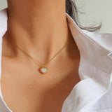 A person wearing the Josie Vintage Heart Pendant Necklace by Flanerie by MAIQ, a vintage heart pendant on a thin gold chain featuring a white center on the charm.